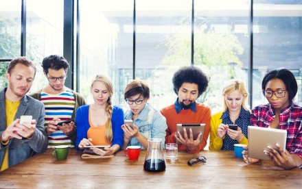 Groupe de jeunes multiethnique qui sont connectés sur des tablettes et téléphones mobiles